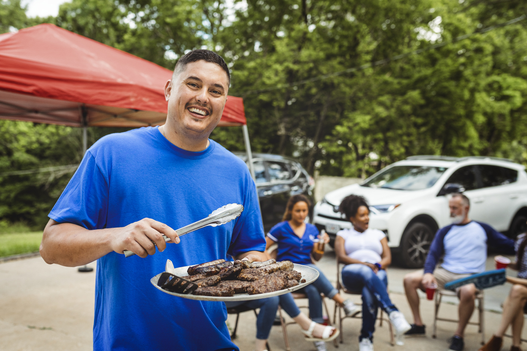 Man handing out burgers at a tailgate party